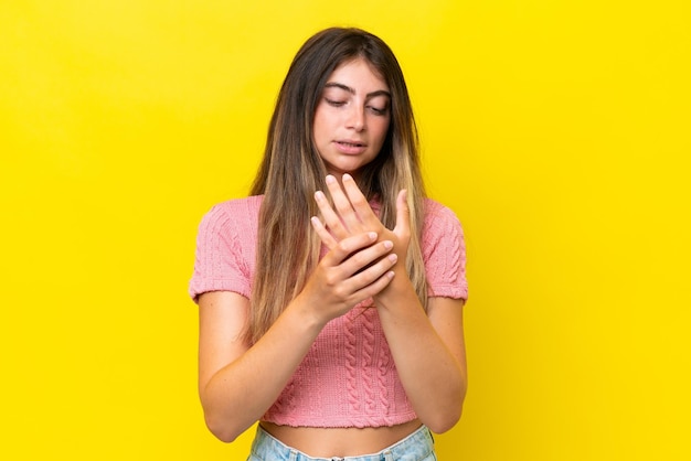 Joven mujer caucásica aislada en fondo amarillo sufriendo dolor en las manos