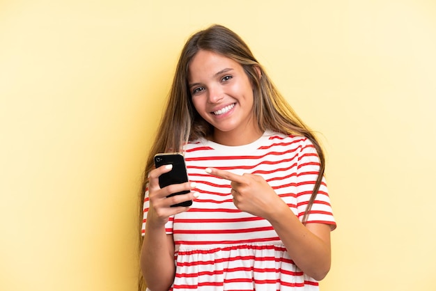 Joven mujer caucásica aislada de fondo amarillo usando un teléfono móvil y apuntándolo