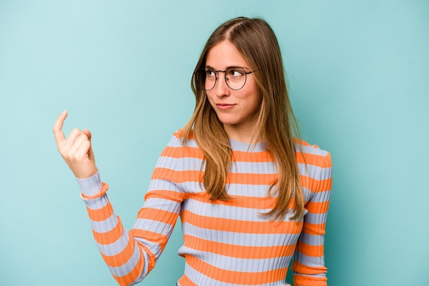 Joven mujer caucásica aislada de fondo azul apuntándote con el dedo como si invitara a acercarse