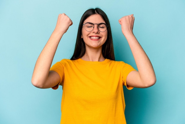 Joven mujer caucásica aislada de fondo azul celebrando una victoria, pasión y entusiasmo, expresión feliz