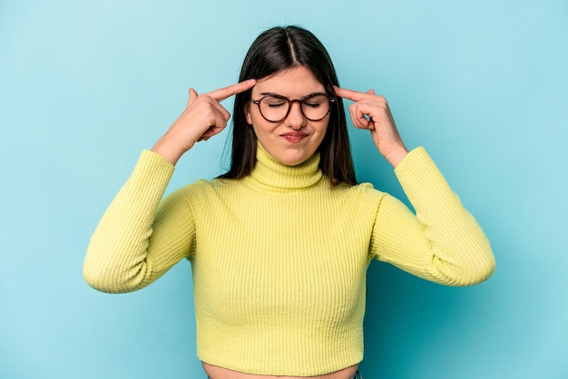 Joven mujer caucásica aislada de fondo azul centrada en una tarea manteniendo los dedos índices apuntando a la cabeza