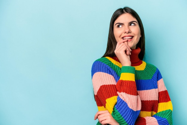 Joven mujer caucásica aislada de fondo azul relajada pensando en algo mirando un espacio de copia