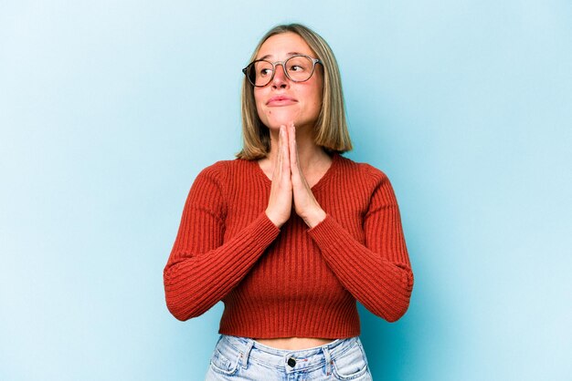 Joven mujer caucásica aislada de fondo azul rezando mostrando devoción persona religiosa en busca de inspiración divina