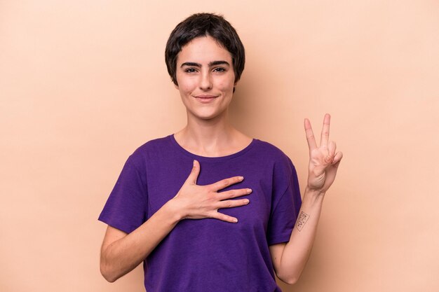 Joven mujer caucásica aislada de fondo beige haciendo un juramento, poniendo la mano en el pecho.