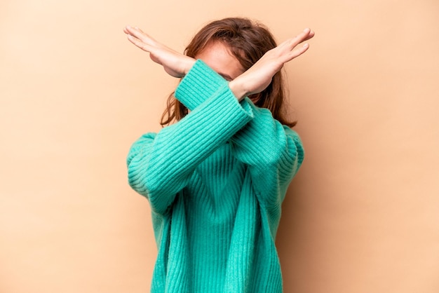 Joven mujer caucásica aislada de fondo beige manteniendo el concepto de negación con dos brazos cruzados