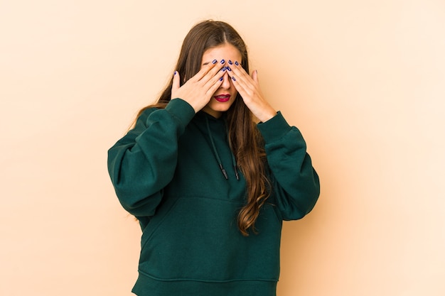 Joven mujer caucásica aislada en fondo beige con miedo cubrirse los ojos con las manos.