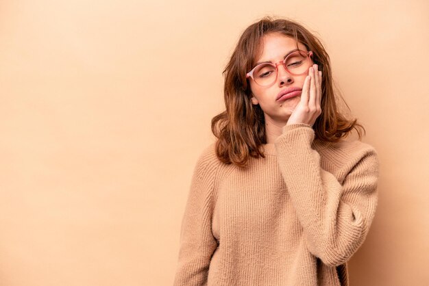 Joven mujer caucásica aislada de fondo beige que se siente triste y pensativa mirando el espacio de la copia