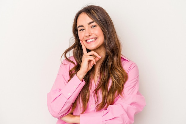 Joven mujer caucásica aislada de fondo blanco sonriendo feliz y confiada, tocando la barbilla con la mano.