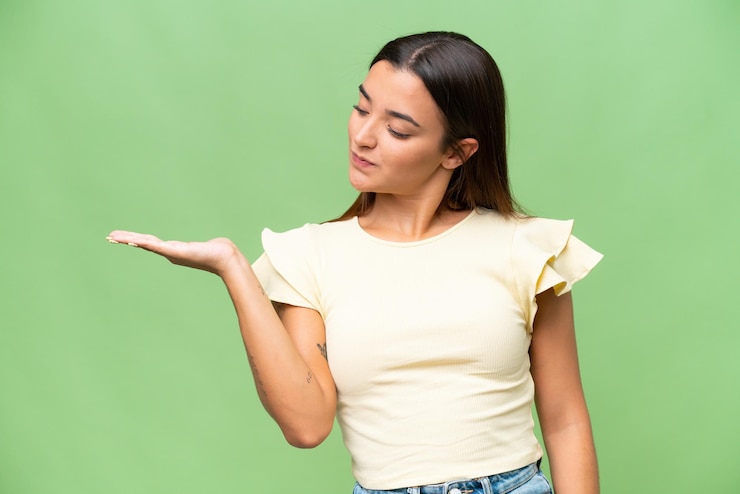 Foto joven mujer caucásica aislada en fondo de croma verde sosteniendo copyspace con dudas