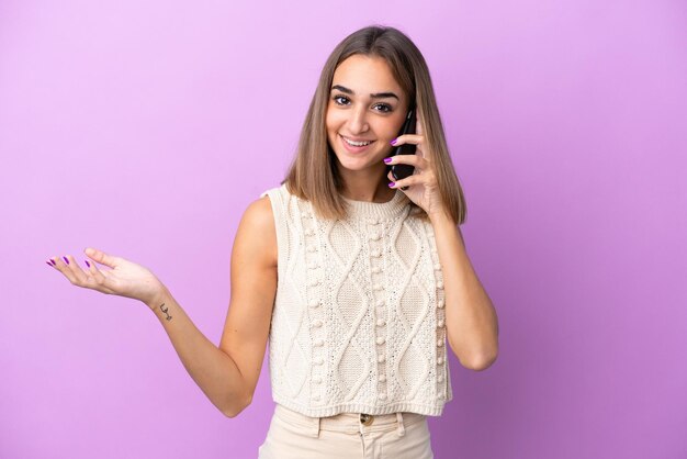 Joven mujer caucásica aislada de fondo morado manteniendo una conversación con alguien por teléfono móvil