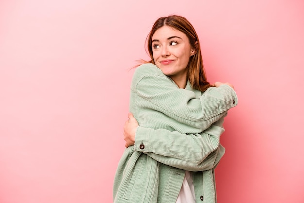 Joven mujer caucásica aislada de fondo rosa abraza sonriendo despreocupada y feliz