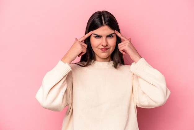 Joven mujer caucásica aislada de fondo rosa centrada en una tarea manteniendo los dedos índices apuntando a la cabeza