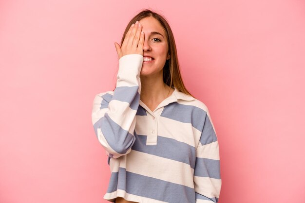 Joven mujer caucásica aislada de fondo rosa divirtiéndose cubriendo la mitad de la cara con la palma