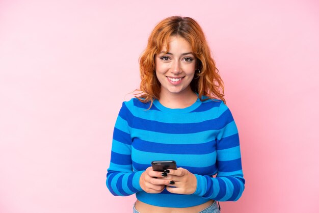 Joven mujer caucásica aislada en fondo rosa enviando un mensaje con el móvil