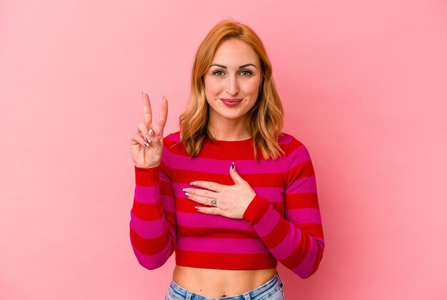 Joven mujer caucásica aislada de fondo rosa haciendo un juramento, poniendo la mano en el pecho.