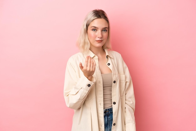 Joven mujer caucásica aislada de fondo rosa invitando a venir con la mano. feliz de que hayas venido