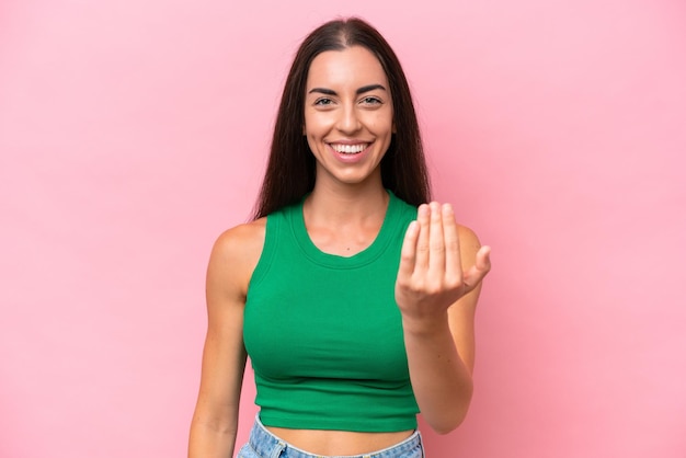 Joven mujer caucásica aislada de fondo rosa invitando a venir con la mano feliz de que hayas venido