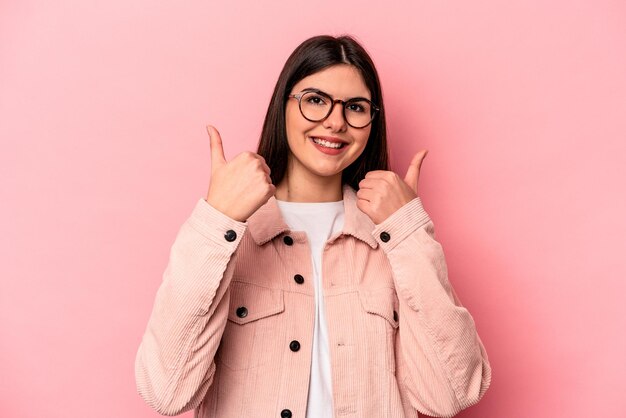 Joven mujer caucásica aislada de fondo rosa levantando ambos pulgares sonriendo y confiada