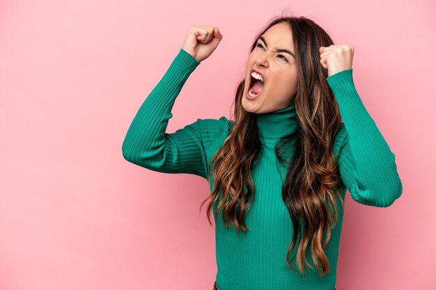 Joven mujer caucásica aislada de fondo rosa levantando el puño después de un concepto de ganador de la victoria