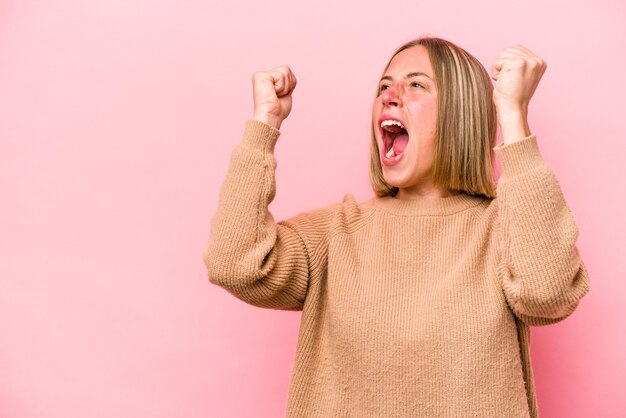 Joven mujer caucásica aislada de fondo rosa levantando el puño después de un concepto de ganador de la victoria