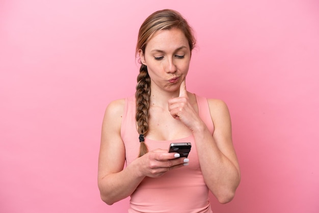 Joven mujer caucásica aislada de fondo rosa pensando y enviando un mensaje