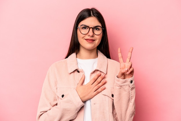 Joven mujer caucásica aislada de fondo rosa prestando juramento poniendo la mano en el pecho