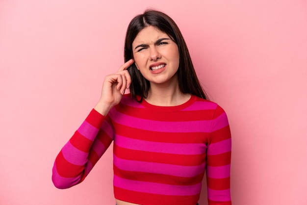 Joven mujer caucásica aislada de fondo rosa que cubre las orejas con los dedos estresada y desesperada por un ambiente ruidoso