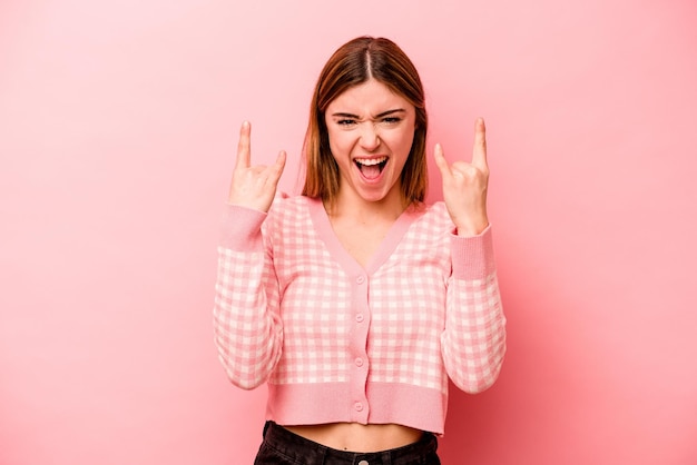 Joven mujer caucásica aislada de fondo rosa que muestra un gesto de cuernos como un concepto de revolución