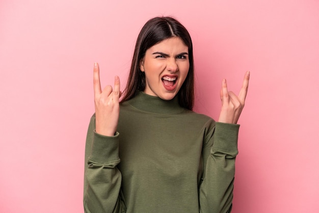 Joven mujer caucásica aislada de fondo rosa que muestra un gesto de cuernos como un concepto de revolución