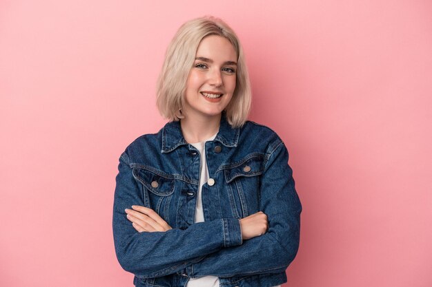 Joven mujer caucásica aislada de fondo rosa que se siente segura, cruzando los brazos con determinación.