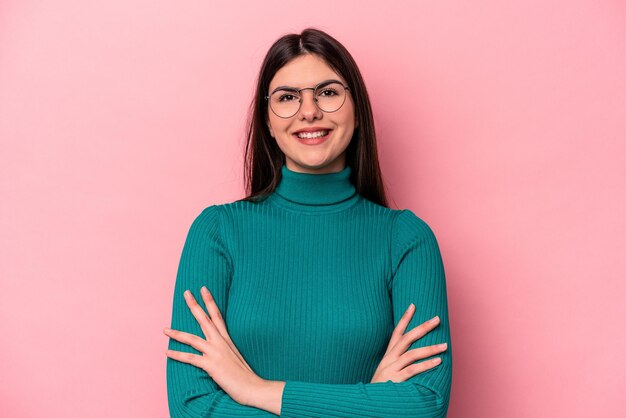 Joven mujer caucásica aislada de fondo rosa que se siente segura cruzando los brazos con determinación