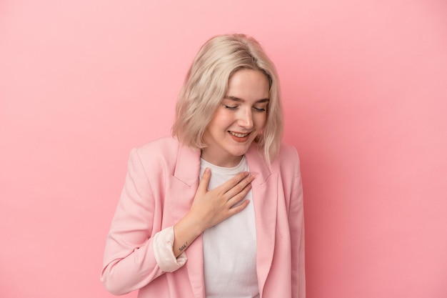 Joven mujer caucásica aislada de fondo rosa riéndose manteniendo las manos en el corazón, concepto de felicidad.