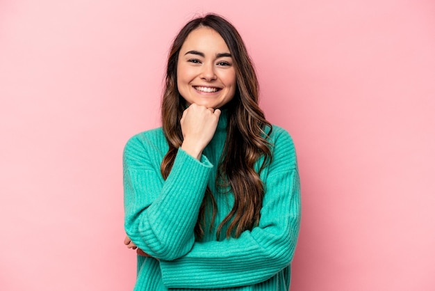 Joven mujer caucásica aislada de fondo rosa sonriendo feliz y confiada tocando la barbilla con la mano