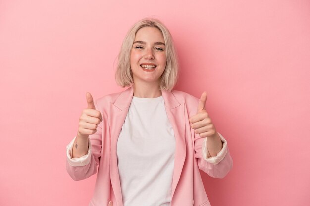 Joven mujer caucásica aislada de fondo rosa sonriendo y levantando el pulgar