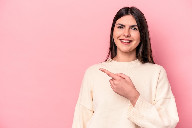 Joven mujer caucásica aislada de fondo rosa sonriendo y señalando a un lado mostrando algo en el espacio en blanco