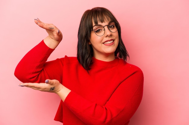 Joven mujer caucásica aislada de fondo rosa sosteniendo algo pequeño con los dedos índices sonriendo y confiada