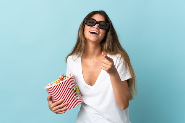 Joven mujer caucásica aislada con gafas 3d y sosteniendo un gran cubo de palomitas de maíz