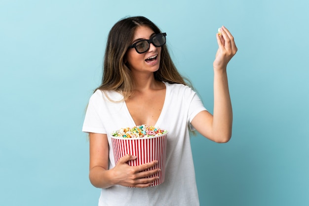 Joven mujer caucásica aislada con gafas 3d y sosteniendo un gran cubo de palomitas de maíz