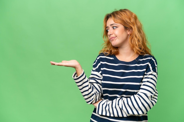 Foto joven mujer caucásica aislada en pantalla verde con fondo de tecla cromática sosteniendo copyspace con dudas