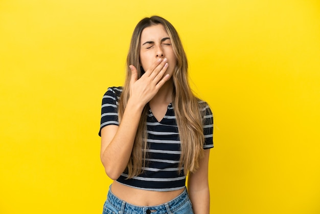 Joven mujer caucásica aislada en la pared amarilla bostezando y cubriendo la boca abierta con la mano
