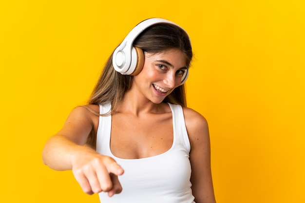 Joven mujer caucásica aislada en la pared amarilla escuchando música