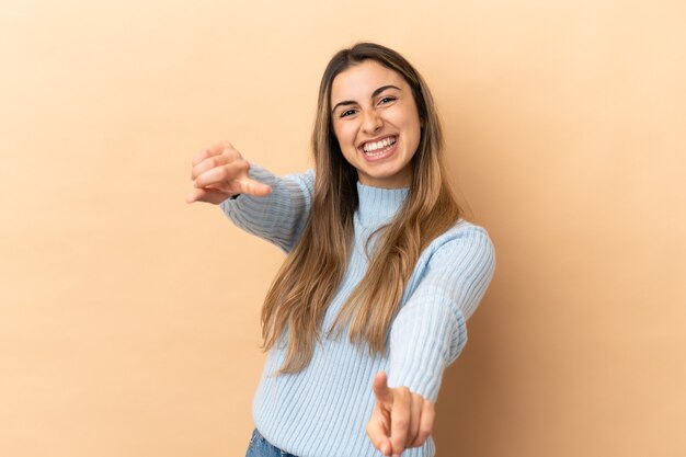 Joven mujer caucásica aislada en la pared beige apuntando al frente con expresión feliz