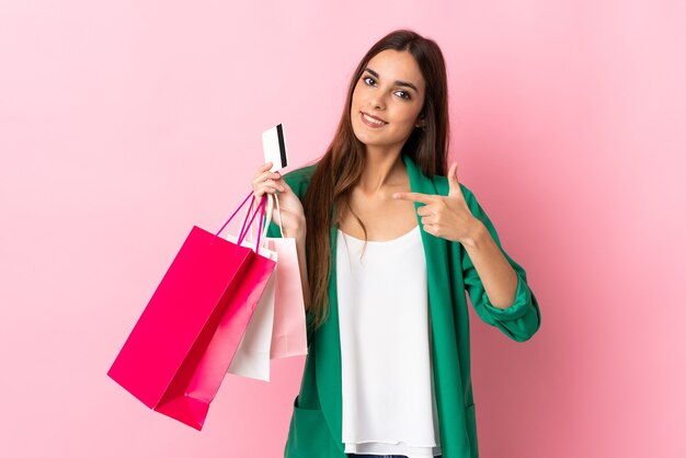 Joven mujer caucásica aislada en la pared rosa con bolsas de la compra y una tarjeta de crédito