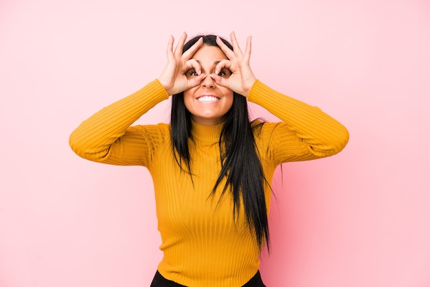 Joven mujer caucásica aislada en una pared rosada mostrando bien firmar sobre los ojos