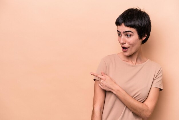 Joven mujer caucásica aislada en puntos de fondo beige con el dedo pulgar lejos, riendo y despreocupada.