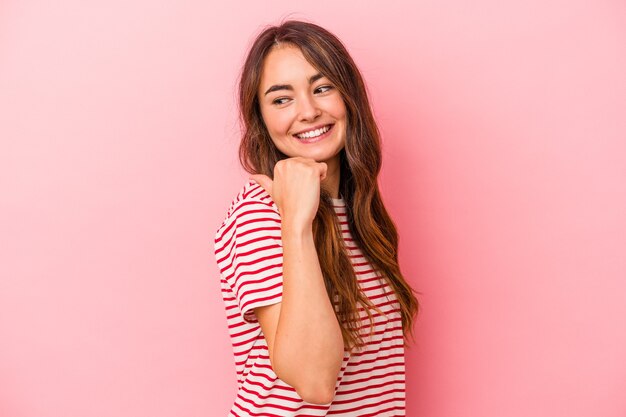 Joven mujer caucásica aislada en puntos de fondo rosa con el dedo pulgar lejos, riendo y sin preocupaciones.