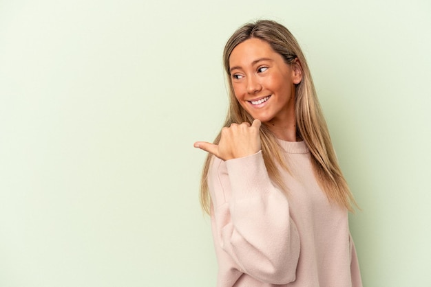 Joven mujer caucásica aislada en puntos de fondo verde con el dedo pulgar lejos, riendo y sin preocupaciones.