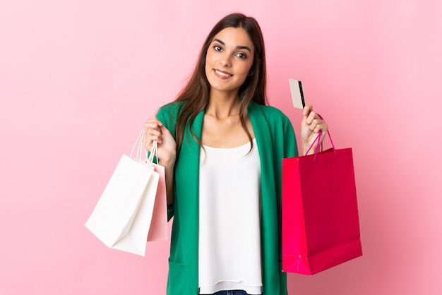 Joven mujer caucásica aislada en rosa sosteniendo bolsas de compras y sorprendido