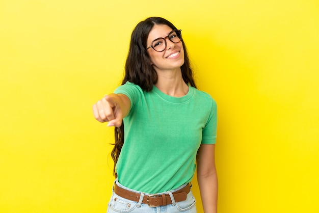 Joven mujer caucásica aislada sobre fondo amarillo apuntando al frente con expresión feliz