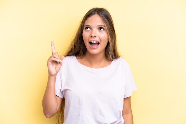 Joven mujer caucásica aislada sobre fondo amarillo apuntando hacia arriba y sorprendido